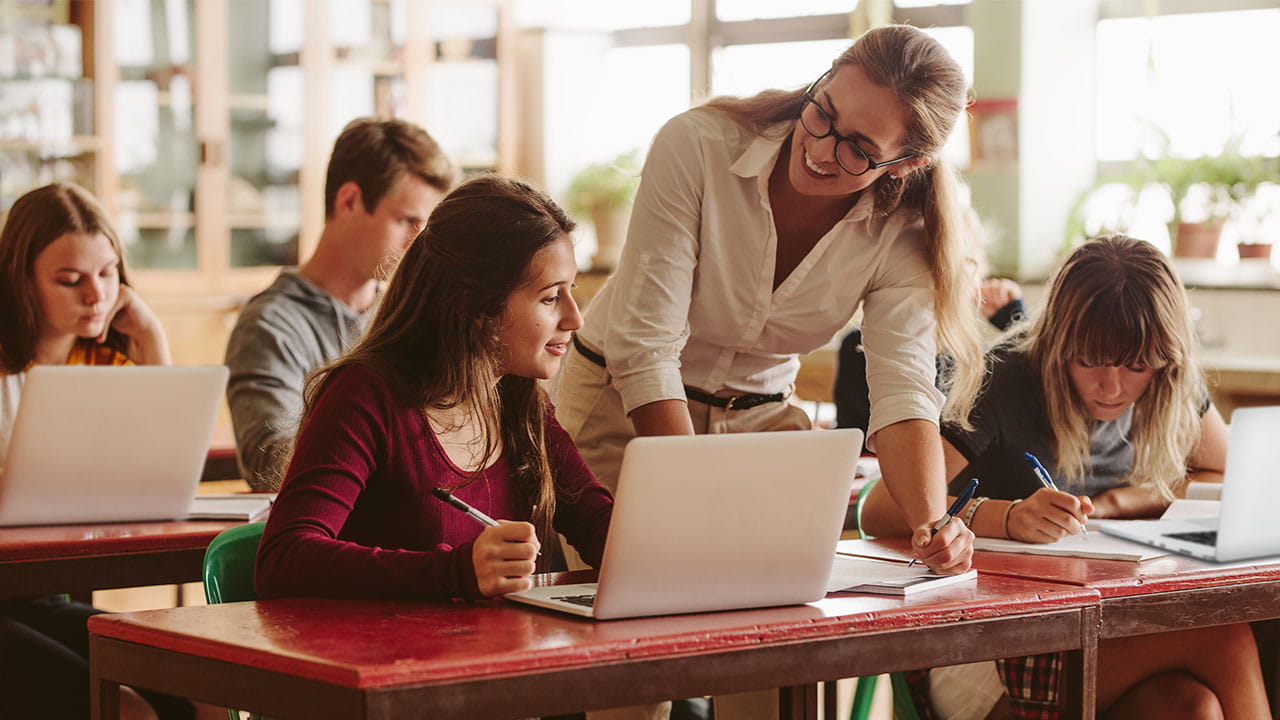 Students working on laptops with the teacher providing support.