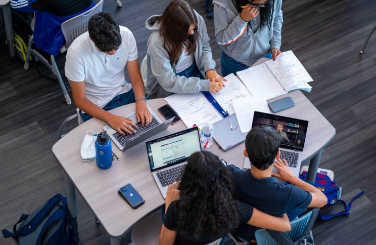 Group of students working on laptops and assignments during a study session.