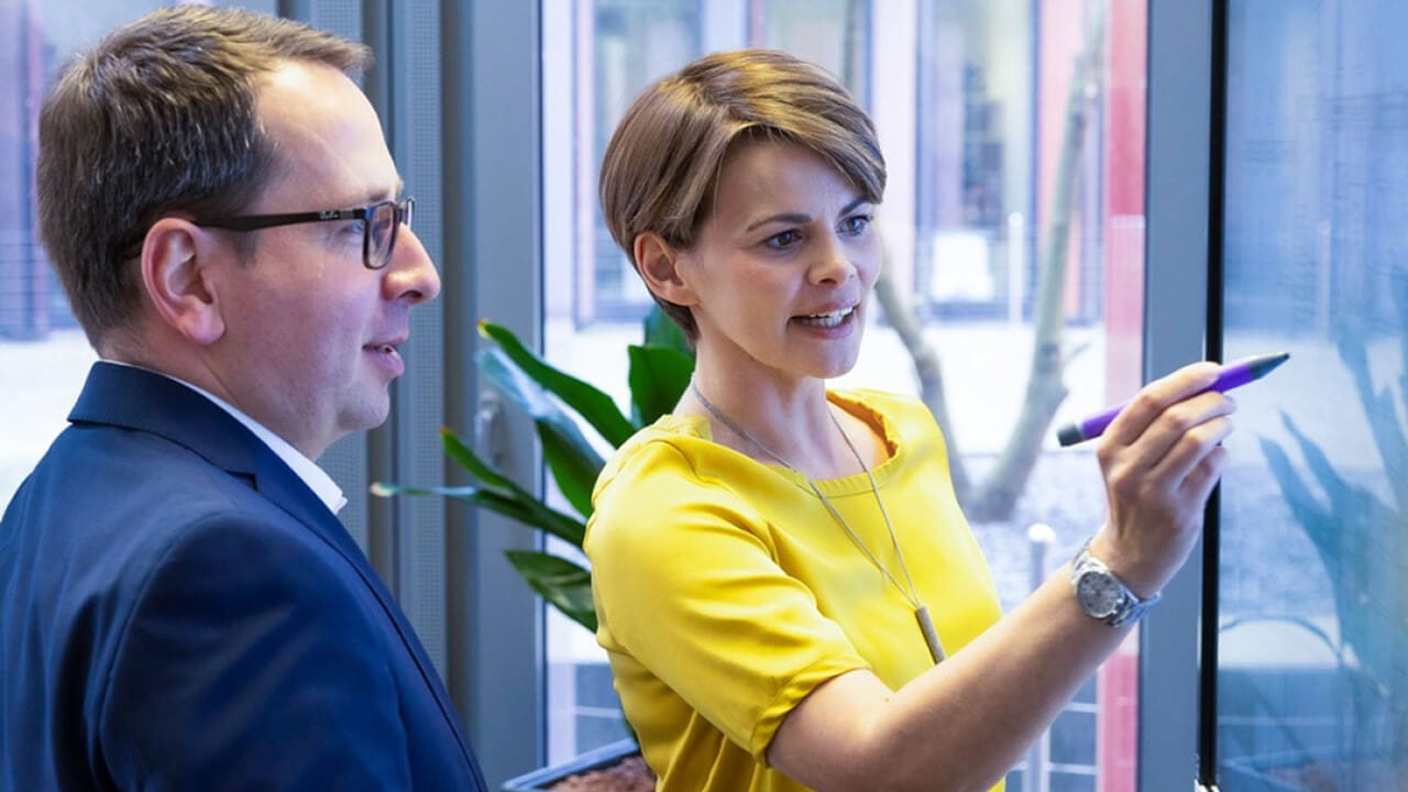 Two professionals standing in front of a SMART board, actively engaged in a collaborative presentation.