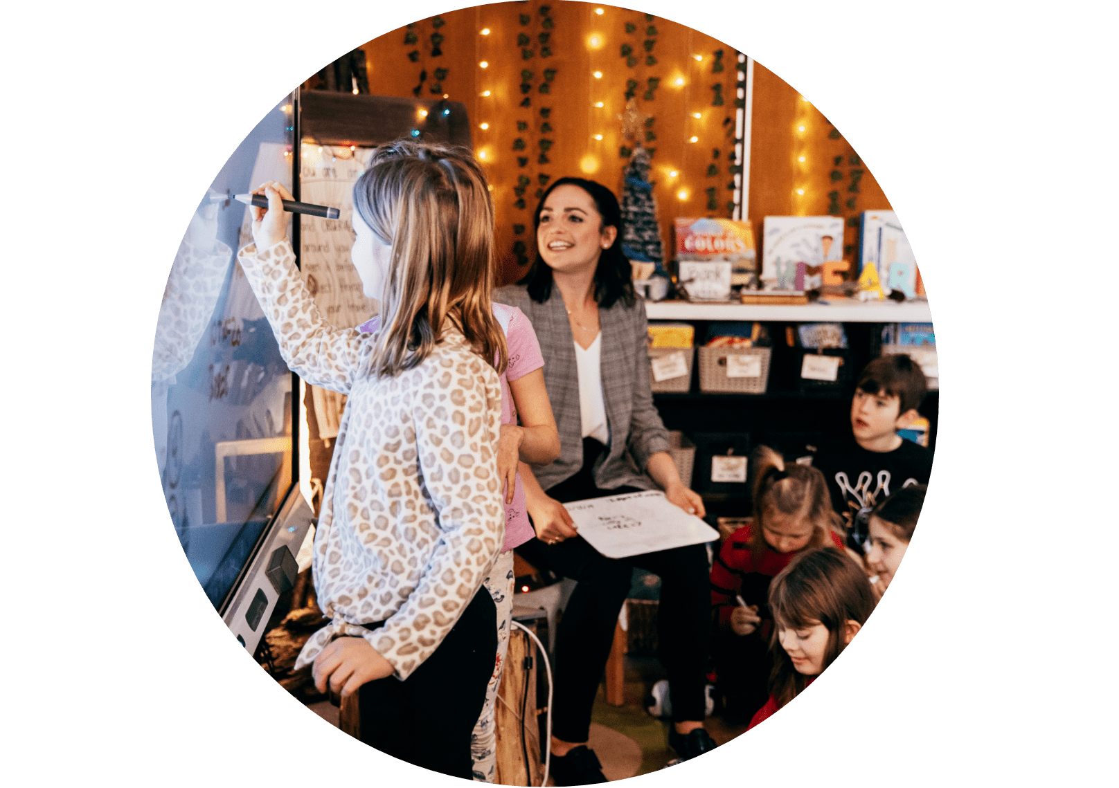 Interactive classroom session where a teacher supports a student interacting with a SMART interactive display, surrounded by engaged children.